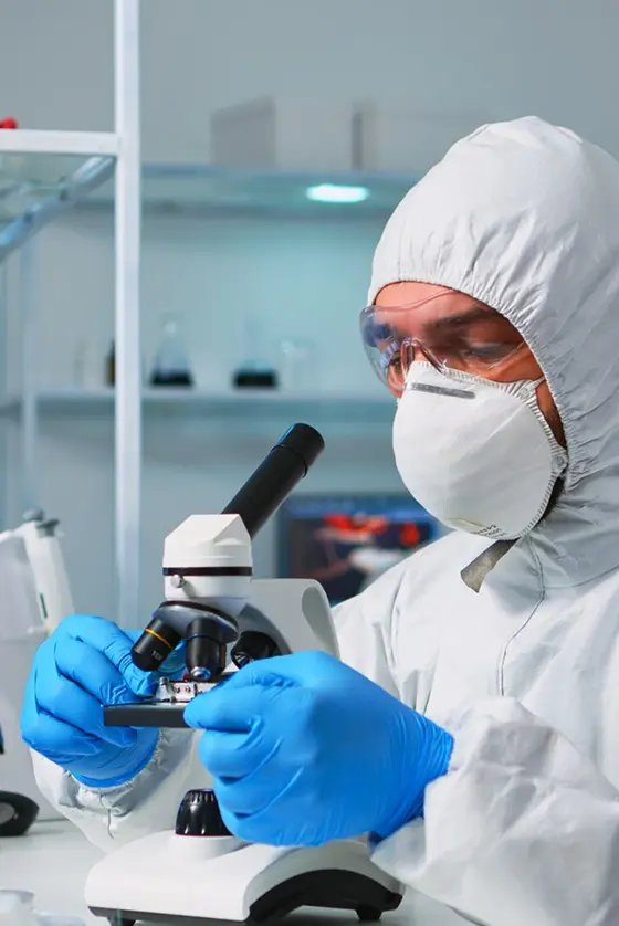Researcher at a microscope in protective equipment